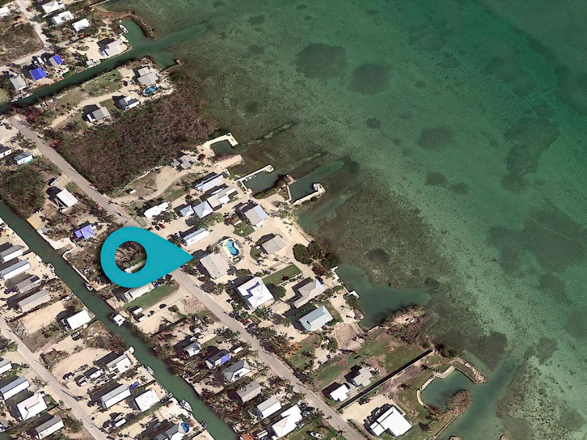 This image shows an aerial view of a coastal community with houses, roads, and docks, next to a body of clear turquoise water.