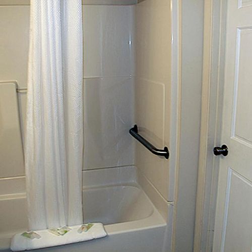 A bathroom with a bathtub and shower curtain, a white sink, a grab bar, and a door with a black handle.