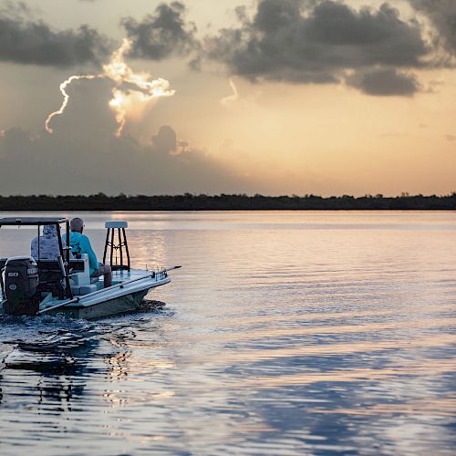 A small boat with two people is navigating calm waters at sunset, with a dramatic sky and a glowing heart-shaped cloud.