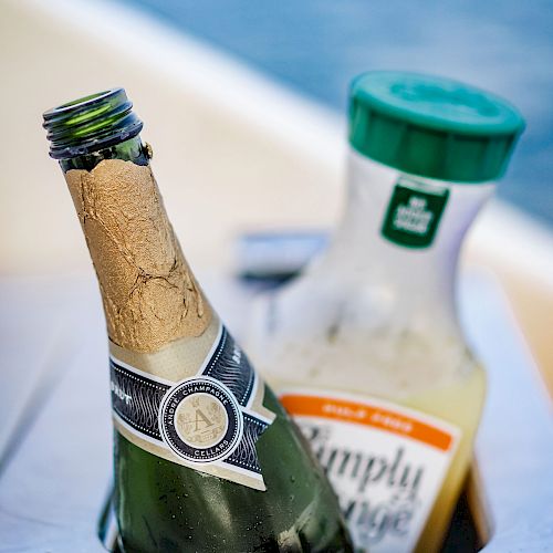 The image shows a bottle of champagne and a container of orange juice placed in a drink holder, likely on a boat.