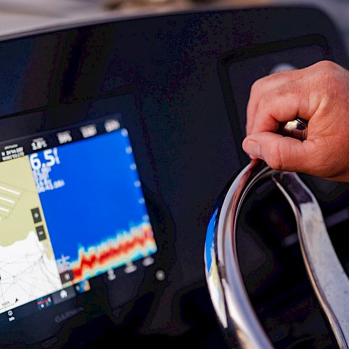 A person is steering a boat while monitoring navigation data on a screen, which displays a map and other information.