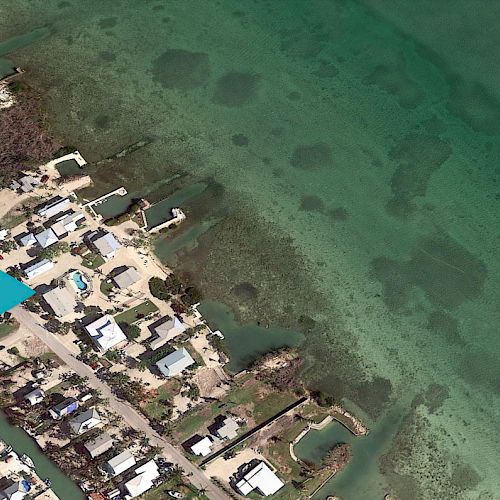 An aerial view of a coastal residential area with turquoise water, small boats, and multiple houses near the shoreline ending the sentence.