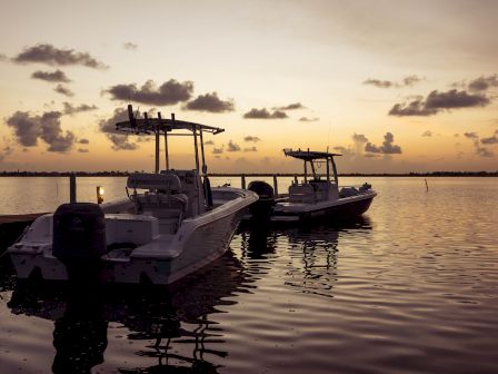 Two boats are docked on a calm water body during sunset, with a partly cloudy sky adding to the serene atmosphere.