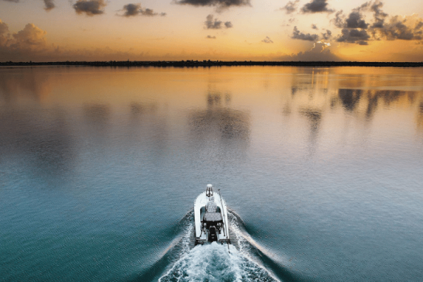 A boat moving across calm waters with a striking orange and cloudy sunset in the background, creating a peaceful and scenic atmosphere.