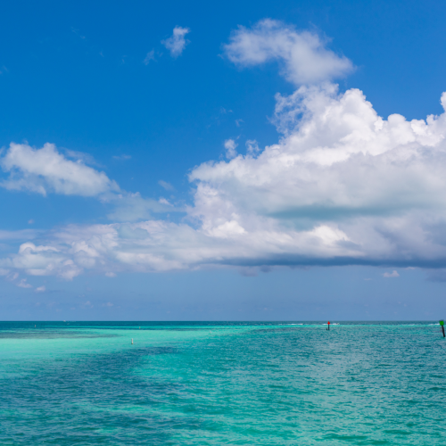 The image shows a serene seascape with turquoise waters, a clear blue sky, and scattered clouds, giving a peaceful and tropical feel.