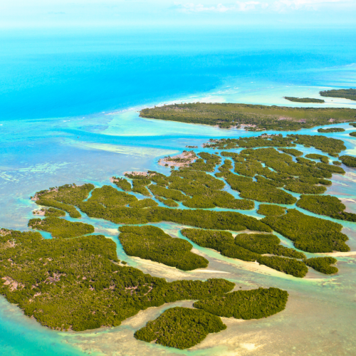 An aerial view of a coastal area with numerous small, lush green islands surrounded by turquoise waters extending out along the shoreline.