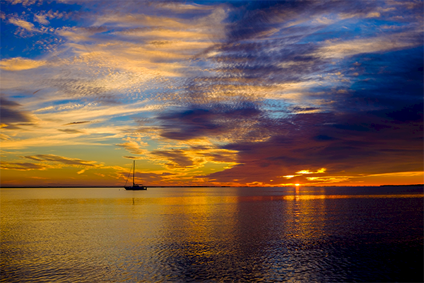 A serene sunset over calm waters, with vibrant colors and a distant sailboat silhouetted against the horizon.