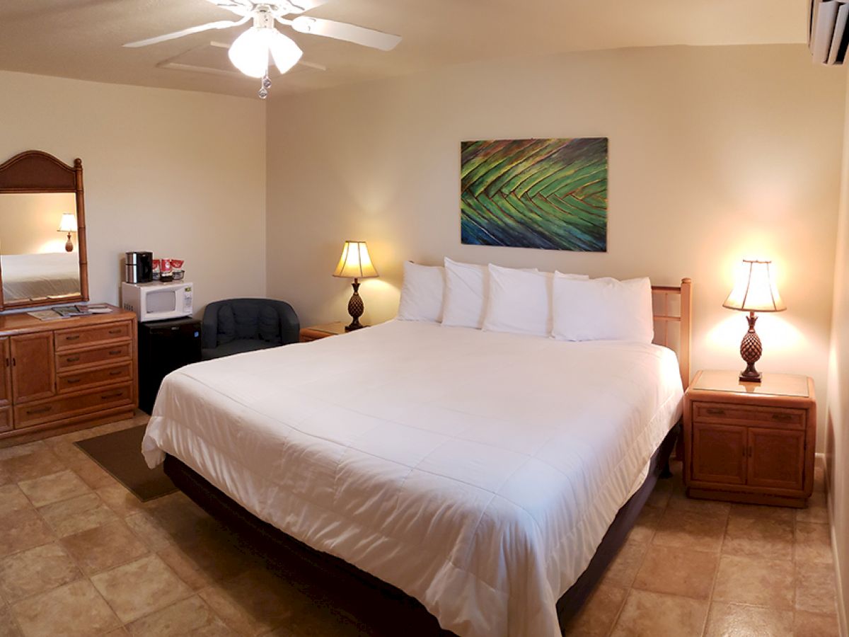 A cozy bedroom with a large bed, two nightstands, lamps, a dresser, mirror, and a small table with a chair, microwave, and coffee maker.