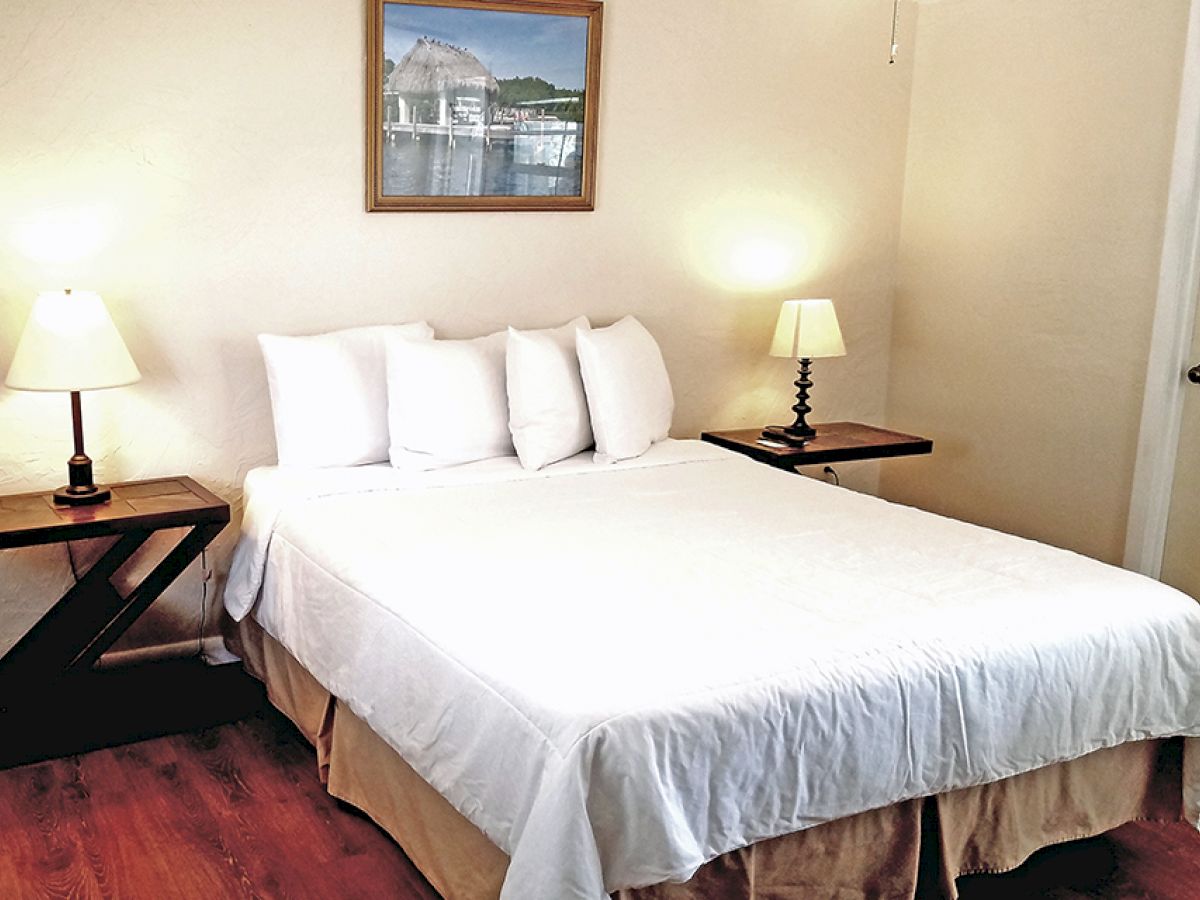 A neatly made bed with white linens is flanked by two nightstands, each with a lamp, in a bedroom featuring a piece of wall art.